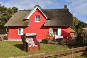 A red house with a thatched roof, a wooden fence, and a garden with a chair. - Holiday home with 2 bedrooms (Born auf dem Darß)