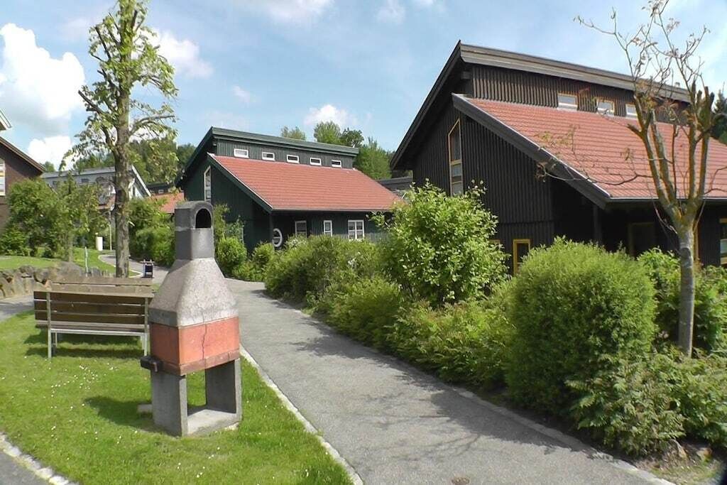 A pathway leading to a building with a red roof, surrounded by greenery and a bench.