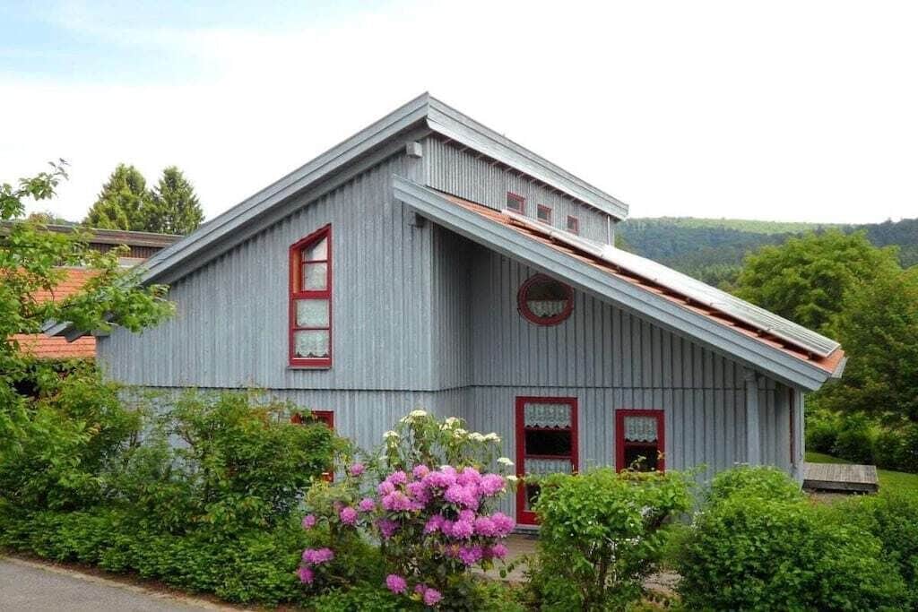 A two-story building with a sloped roof, red-framed windows, and a small porch area.