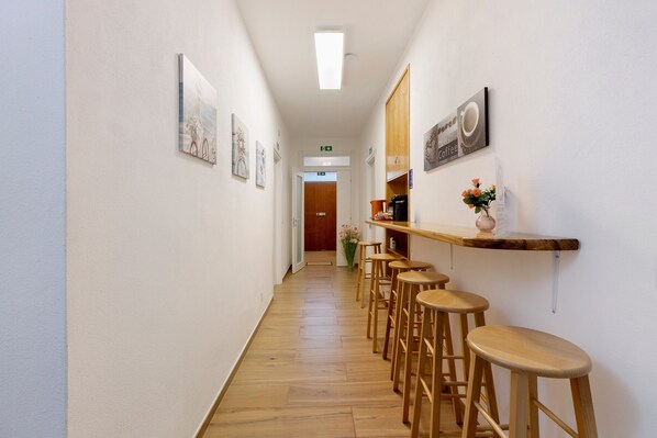 A hallway with wooden flooring, a coffee bar with stools, and framed artwork on the walls.