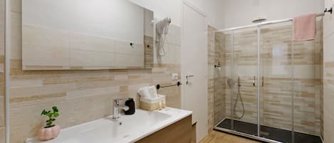A modern bathroom with a large mirror, a vanity with a sink, a shower enclosure, and a potted plant.
