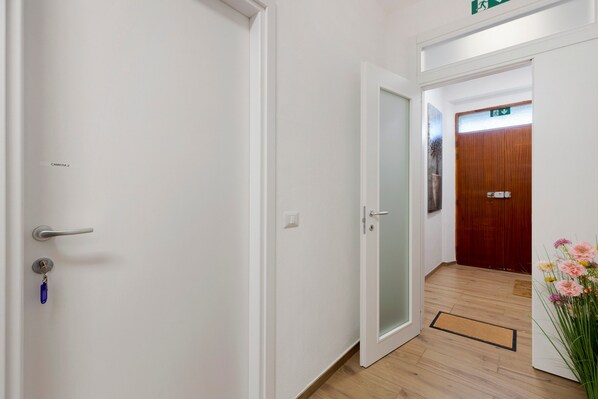 Un couloir avec une porte blanche, une porte en bois et un paillasson.