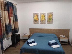 A hotel room with a bed, two bedside tables, a nightstand, a wall-mounted artwork, and a window with curtains. - Room 'Camera Doppia- Da Tea Affittacamere' with Mountain View, Wi-Fi and Air Conditioning (Olzai)