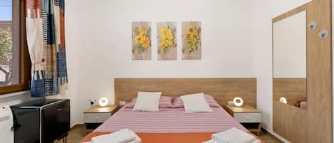 A hotel room with a bed, two bedside tables, a desk, and a chair. There are three wall art pieces above the bed.