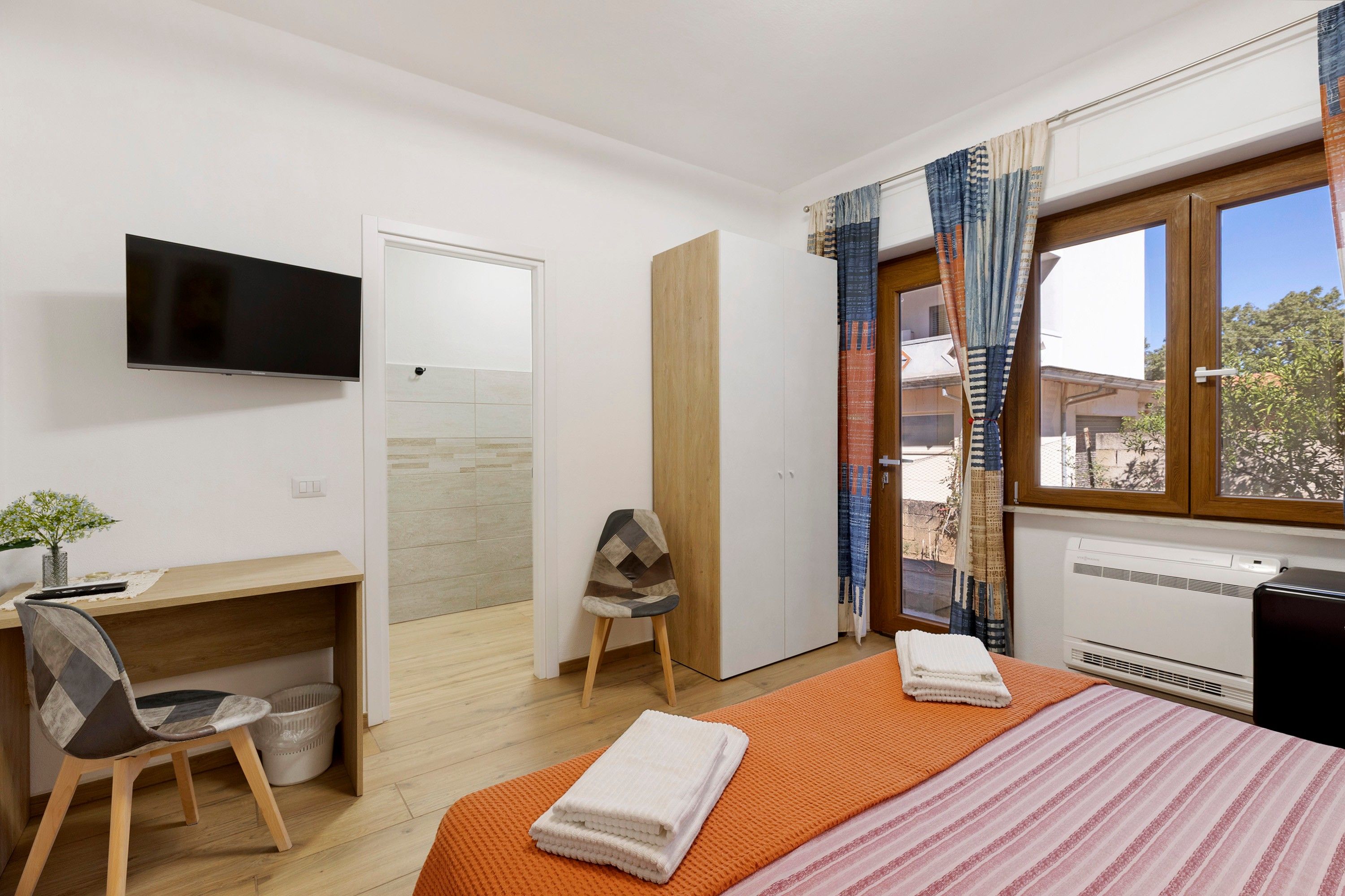 A hotel room with a bed, a desk, a chair, a TV, and a window with curtains.