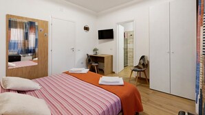 A hotel room with a bed, a desk, a chair, a television, and a shower area.