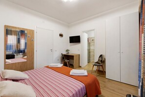 A hotel room with a bed, a desk, a chair, a television, and a shower area.