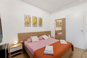 A bedroom with a wooden headboard, a bed with pink striped bedding, a nightstand with a lamp, and a wall with three floral artwork pieces.