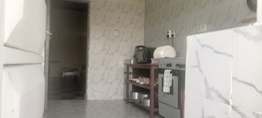 A kitchen with a microwave, stove, and shelves with pots.