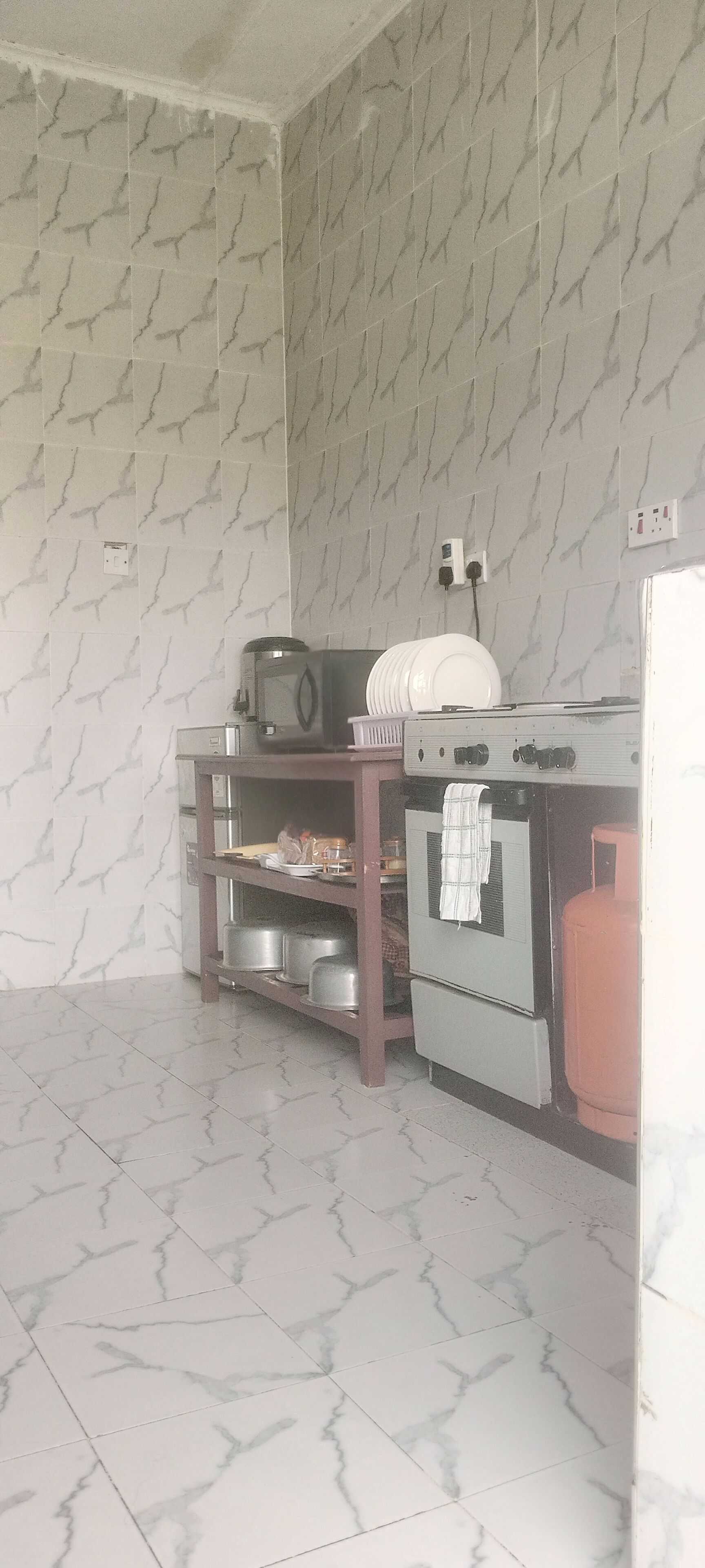 Una cocina con salpicadero de azulejos, estufa, lavamanos y encimera con diversos utensilios de cocina.