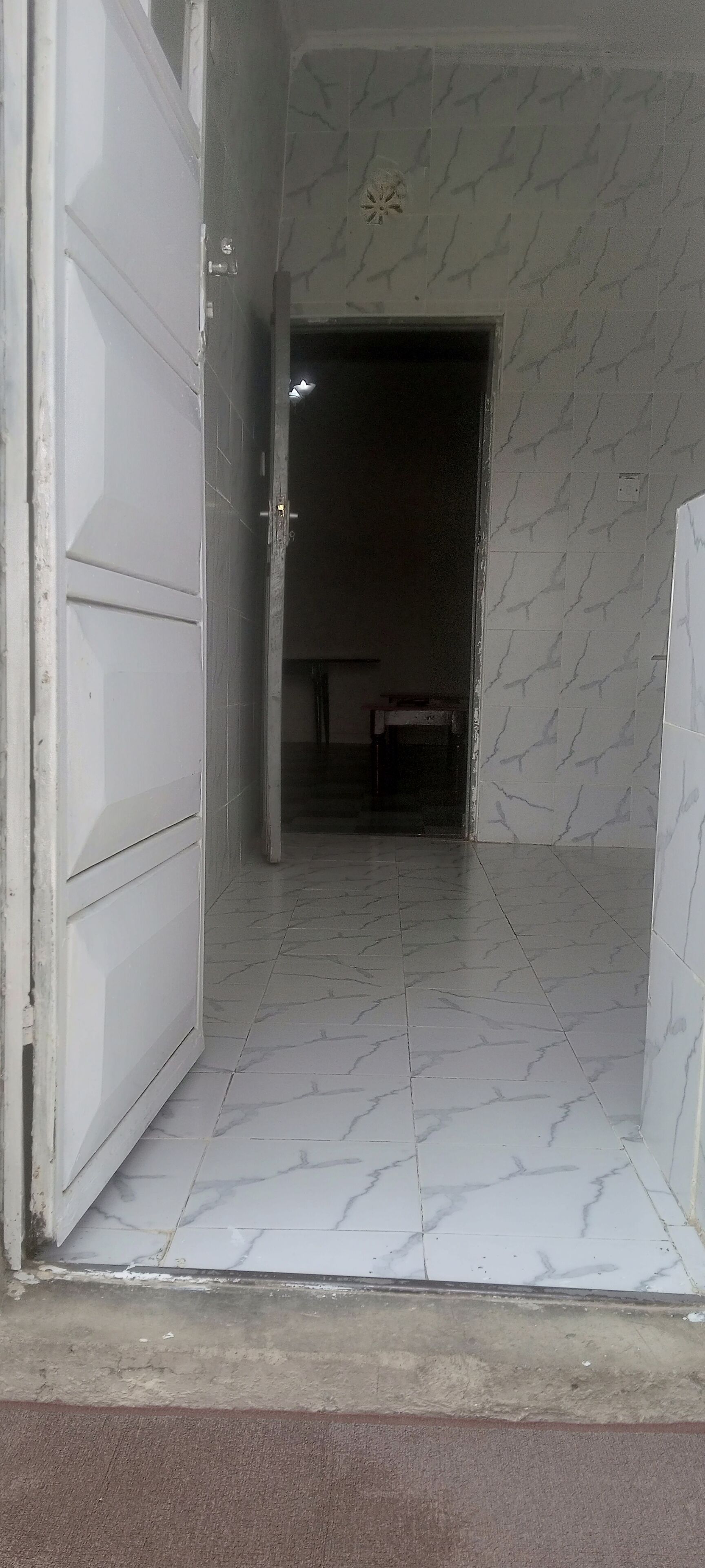A hallway with a marble floor leading to a dark room.