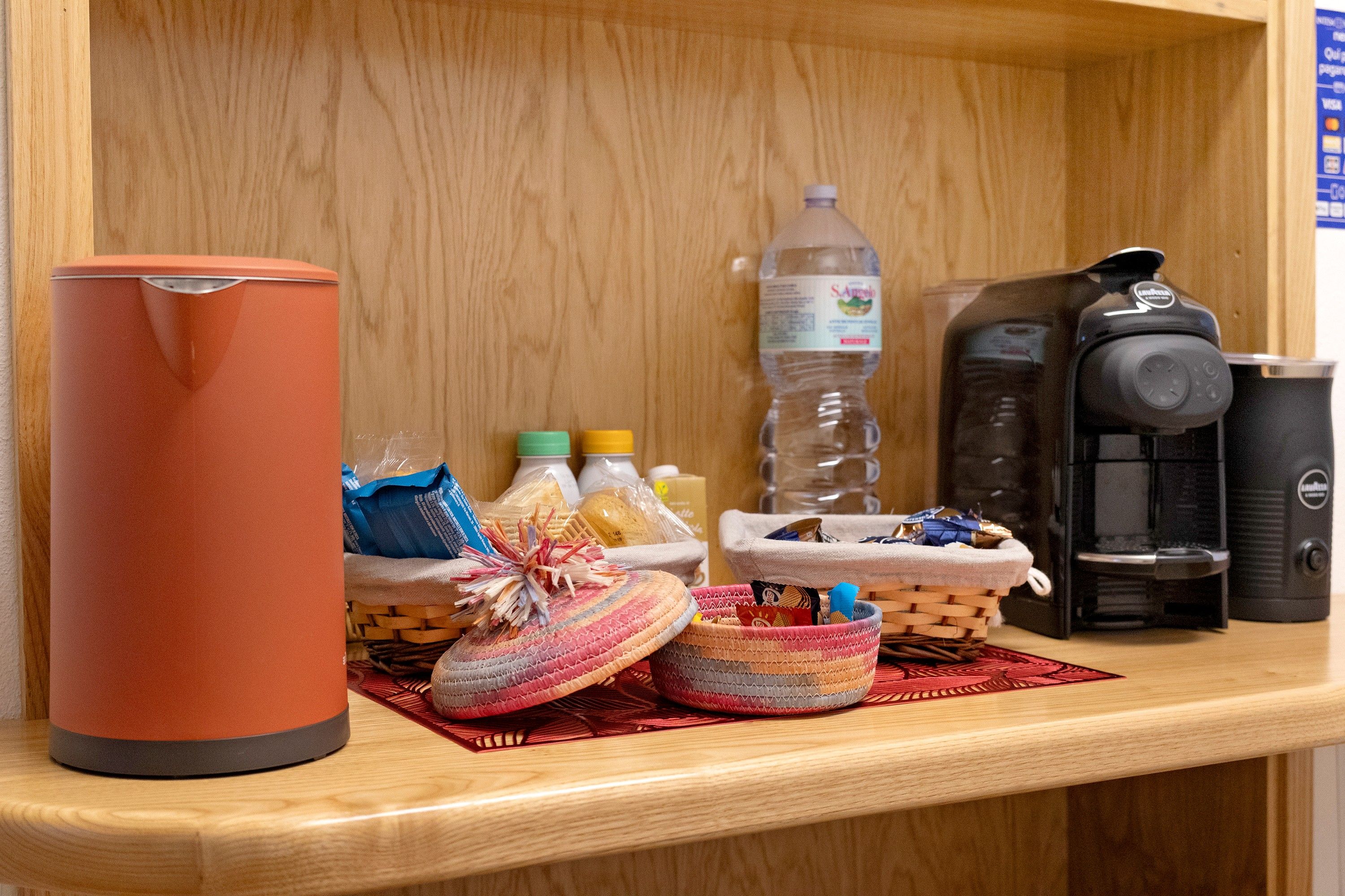 Ein Regal mit Thermoskanne, Wasserflaschen, Kaffeemaschine und Körben voller Snacks.