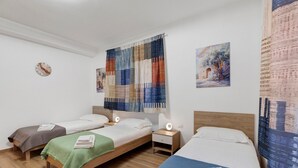 A room with two single beds, a nightstand with a lamp, a wall clock, and a large abstract painting.