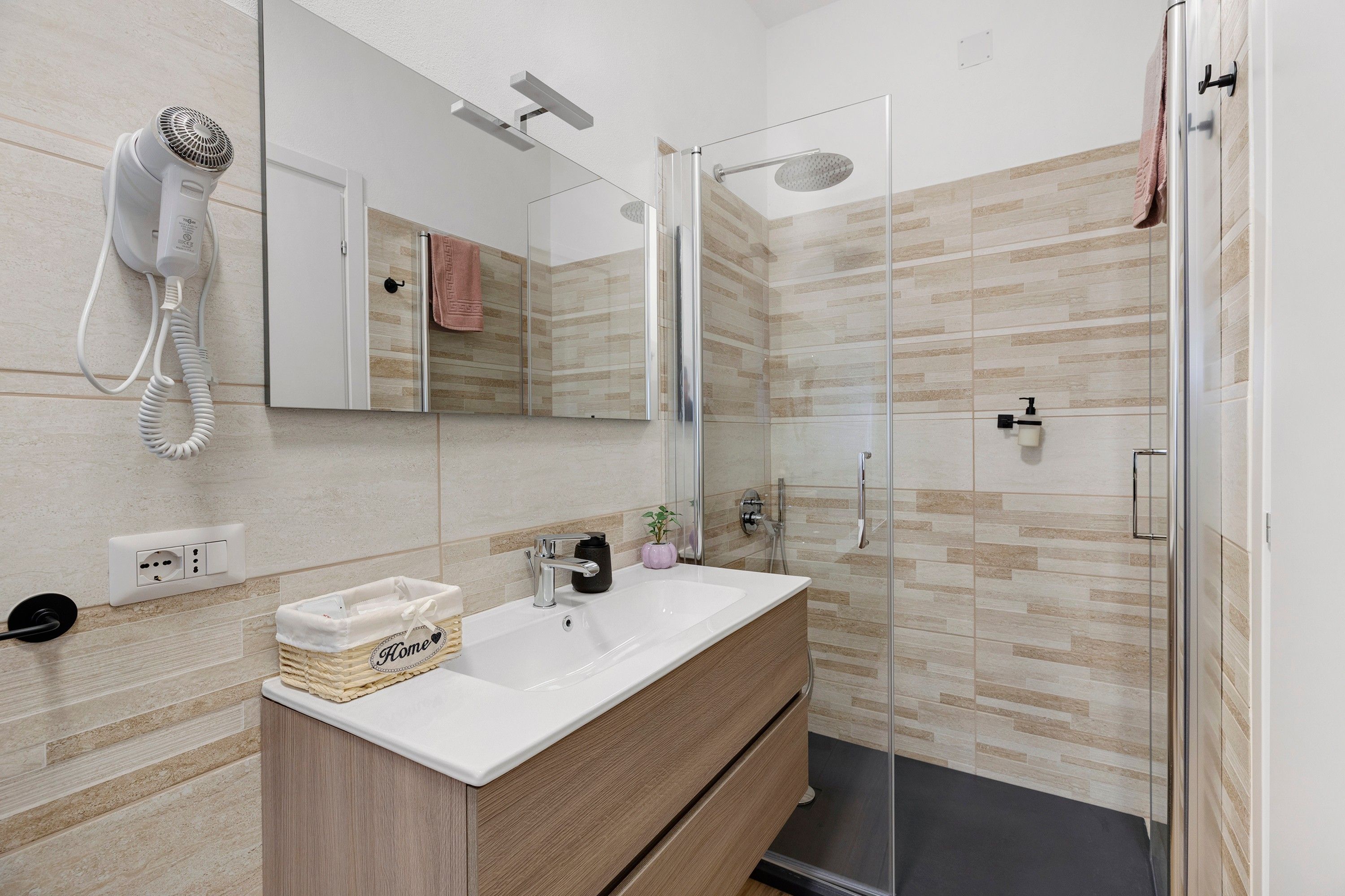 Une salle de bain moderne avec une douche à parois de verre, un lavabo blanc et un sèche-cheveux fixé au mur.
