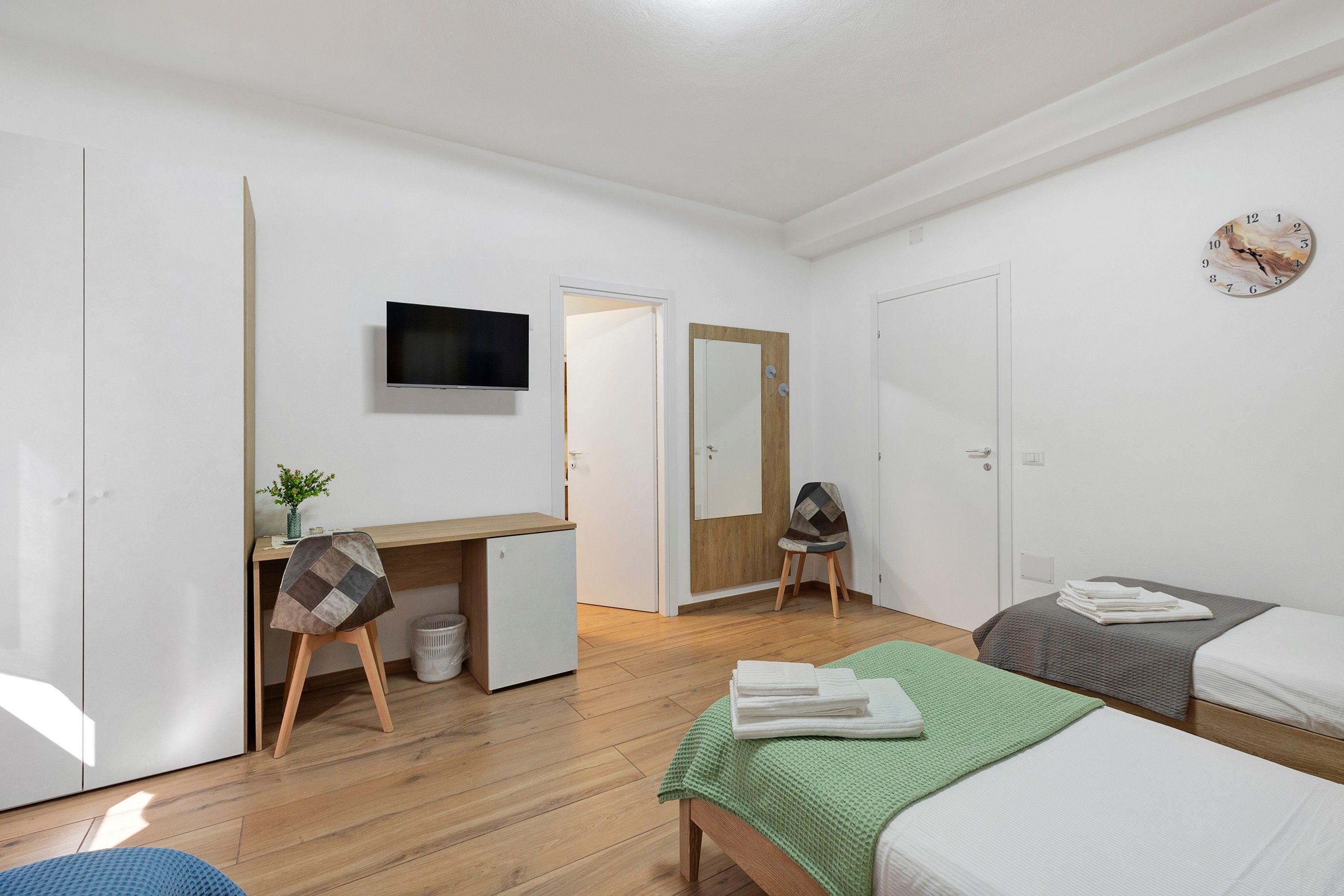A compact room with a bed, a desk, a chair, a television, and a clock on the wall.