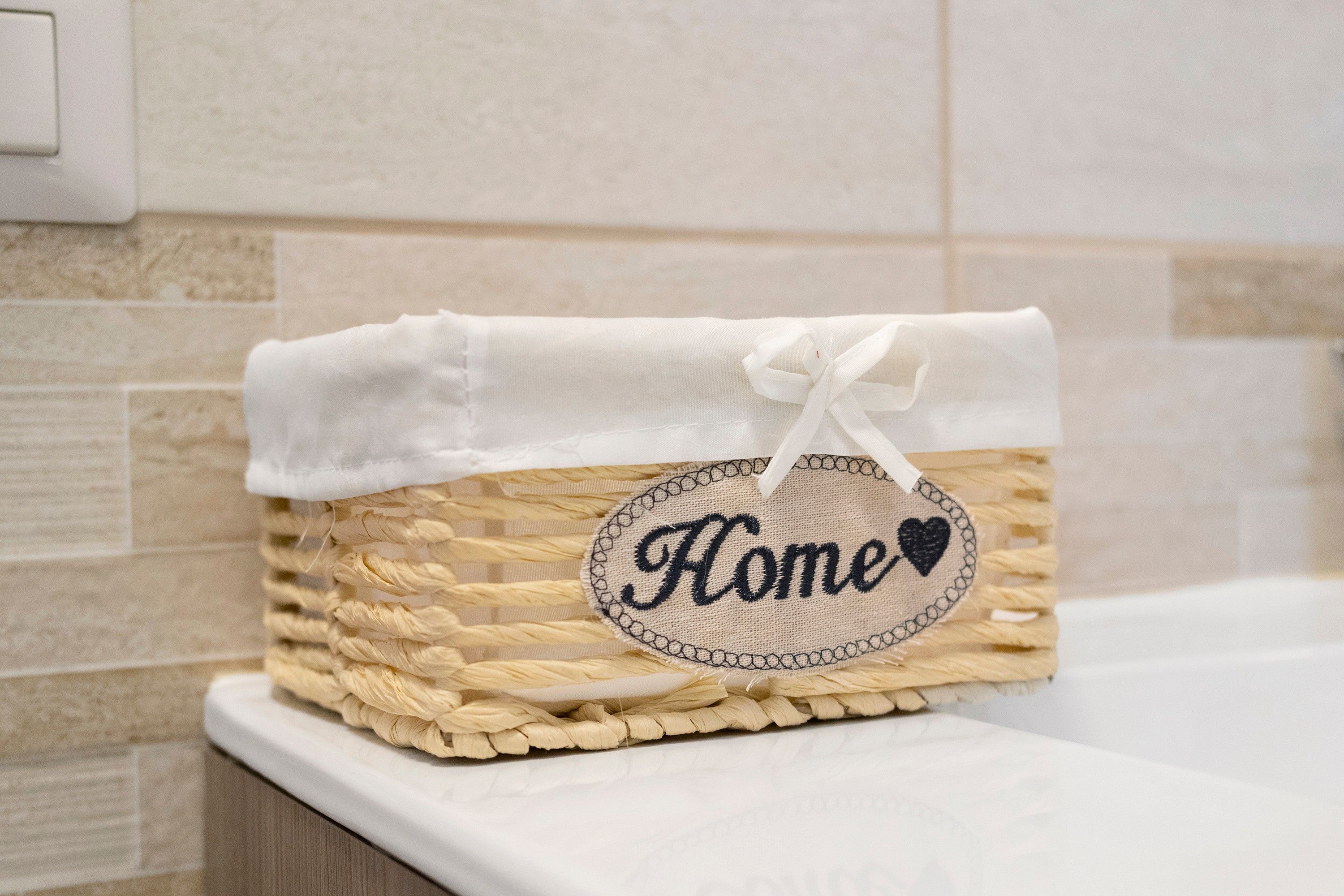 Ein gewebter Korb mit weißem Stoffüberzug und einem Schildchen mit der Aufschrift 'Home' und einem Herzsymbol.