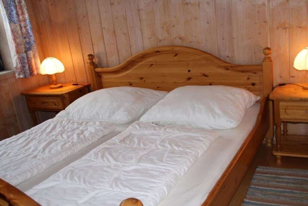 A wooden bed with white bedding in a room with wooden walls and two bedside lamps.