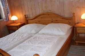 Ein hölzernes Bett mit weißer Bettwäsche in einem Raum mit Holzwänden und zwei Nachttischlampen.