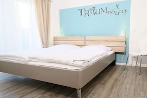Een bed met houten hoofdbord, een muur met een decoratief bord en een witte stoel.