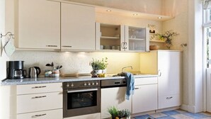 A kitchen with white cabinets, a stove, and a sink. There are plants on the counter and a bag of groceries. - Holiday home with 1 bedroom (Groß Zecher)