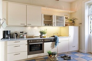 A kitchen with white cabinets, a stove, and a sink. There are plants on the counter and a bag of groceries. - Holiday home with 1 bedroom (Groß Zecher)