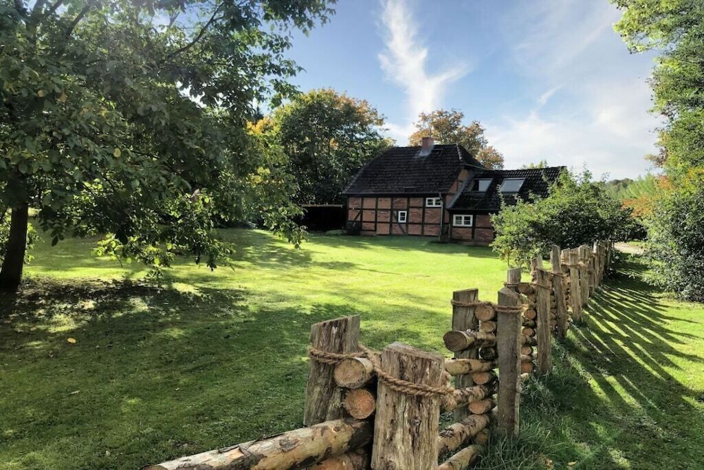 A traditional half-timbered house with a sloped roof, surrounded by a well-maintained lawn and a wooden fence.