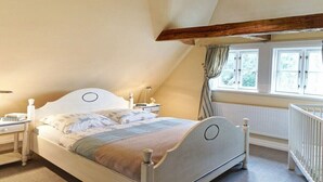 A bedroom with a sloped ceiling, a bed with a headboard, bedside tables, a window with curtains, and a radiator. - Holiday home with 1 bedroom (Groß Zecher)