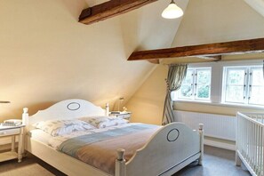 A bedroom with a sloped ceiling, a bed with a headboard, bedside tables, a window with curtains, and a radiator. - Holiday home with 1 bedroom (Groß Zecher)