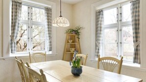 A dining room with a wooden table, four chairs, a hanging light fixture, and a window with curtains. - Holiday home with 1 bedroom (Groß Zecher)