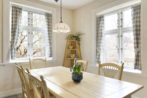 A dining room with a wooden table, four chairs, a hanging light fixture, and a window with curtains. - Holiday home with 1 bedroom (Groß Zecher)