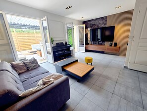 A modern living room with a sofa, coffee table, and a TV area with a wooden accent wall. - Holiday Home “Chez Elie!” with Private Terrace, Garden, and Wi-Fi (Orléans)