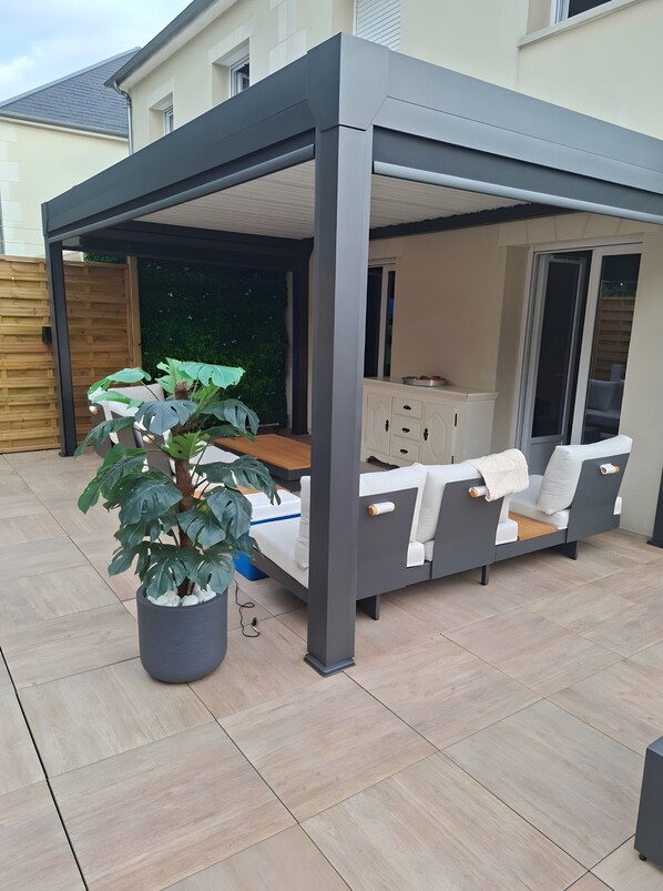 A covered patio area with a sofa, a dining table, and a potted plant. - Holiday Home “Chez Elie!” with Private Terrace, Garden, and Wi-Fi (Orléans)