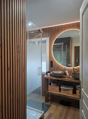 A modern bathroom with a wooden slat wall, a glass shower enclosure, and a vanity with a large mirror. - Holiday Home “Chez Elie!” with Private Terrace, Garden, and Wi-Fi (Orléans)