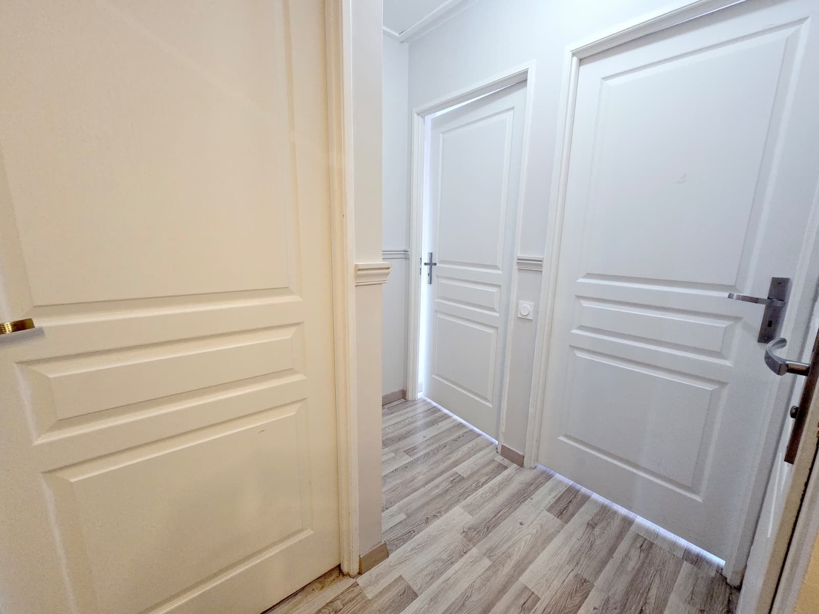 Un couloir avec des portes blanches et un plancher en bois.