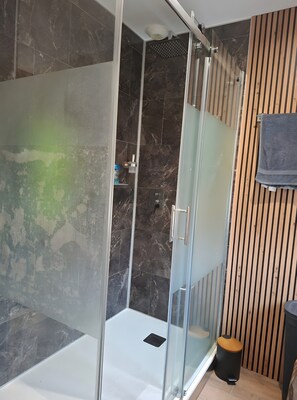 A glass-enclosed shower with a marble wall, a wooden panel wall, and a towel hanging on the right. - Holiday Home “Chez Elie!” with Private Terrace, Garden, and Wi-Fi (Orléans)