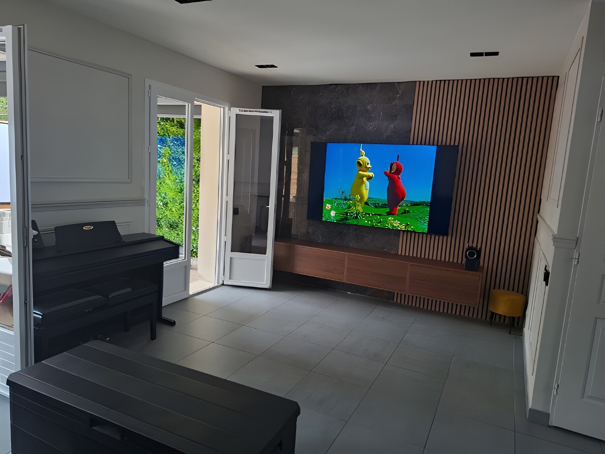 Una sala moderna con una televisión de pantalla plana montada en la pared, un piano y un ventanal corredero que da a un balcón.