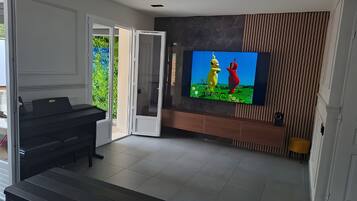 Una sala moderna con una televisión de pantalla plana montada en la pared, un piano y un ventanal corredero que da a un balcón.