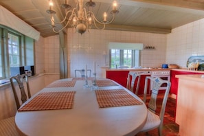 Ein Essbereich mit einem runden Tisch, Stühlen, einer Chandelüster und einer Küche im Hintergrund.