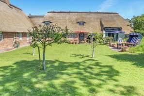 A thatched-roof building with a lawn and outdoor seating area. - Friesenhaus Sara (S2) (Wenningstedt)