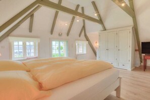 A bedroom with a sloped ceiling, a bed with pillows, a wardrobe, and a television. - Friesenhaus Sara (S2) (Wenningstedt)