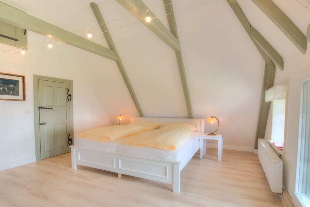Une chambre à coucher avec un lit blanc, une table de chevet avec une lampe, un radiateur et une porte avec une poignée.