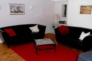 Ein Wohnzimmer mit zwei schwarzen Sofas, einem roten Teppich, einem kleinen Holztisch und einer weißen Lampe.
