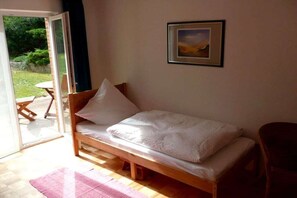 Ein Einzelbett mit Holzrahmen und weißer Bettwäsche in einem Zimmer mit Glastür zu einem Außenbereich.