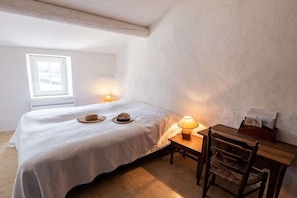 Ein Schlafzimmer mit einem Bett, Nachttischlampen, einem hölzernen Stuhl, einem kleinen Tisch und einem Fenster.