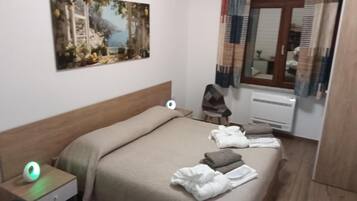 A hotel room with a bed, a bedside table with a lamp, a painting on the wall, and a window with curtains.