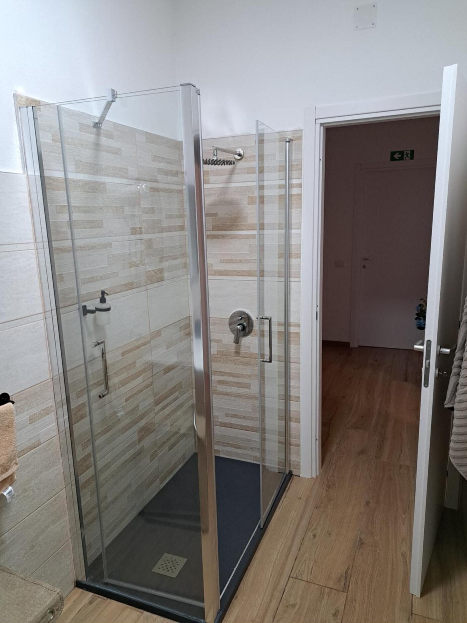 A glass-enclosed shower with a tiled wall and a wooden floor.