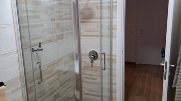 A glass-enclosed shower with a tiled wall and a wooden floor.