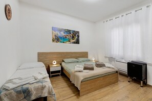 A bedroom with a wooden bed, a bedside table with a lamp, a wall-mounted clock, and a painting.