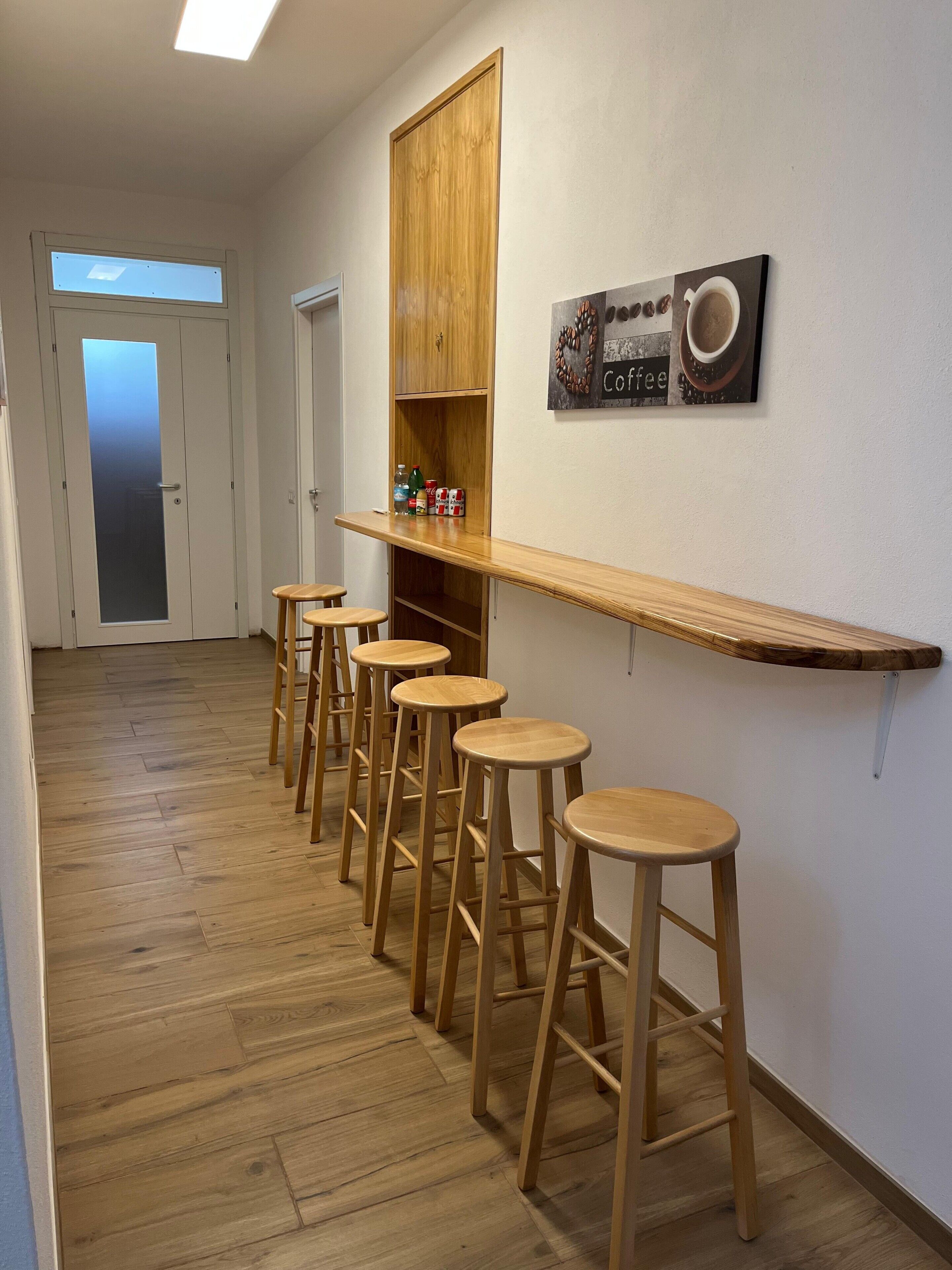 A hallway with wooden flooring, a bar area with stools, and a coffee-themed wall decoration.