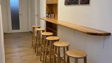A hallway with wooden flooring, a bar area with stools, and a coffee-themed wall decoration.